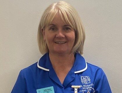 Julie Kirton, Living Well Services Nurse at St Richard's Hospice, smiles and is wearing a blue nurses' uniform.