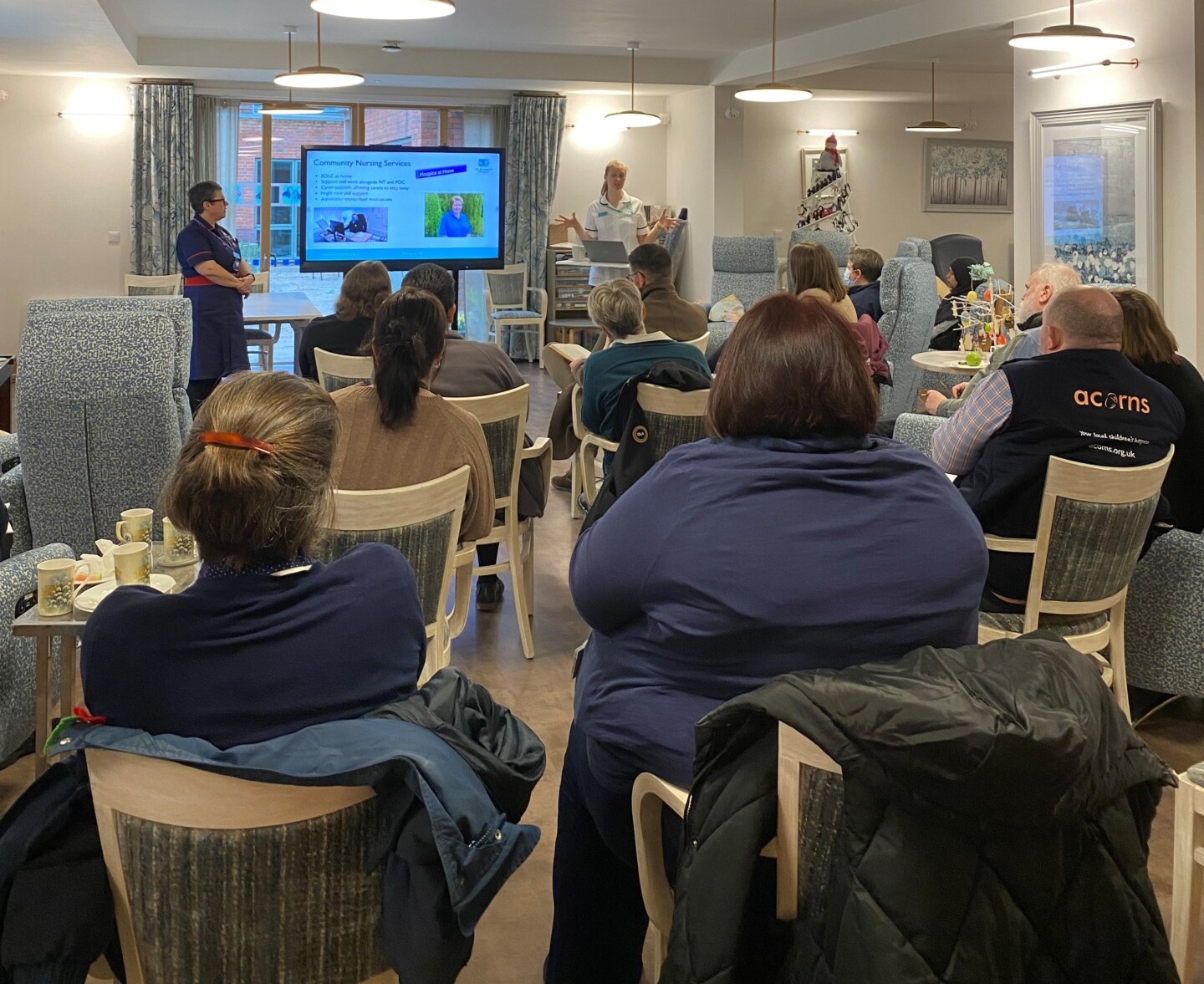 A group of people sit watching a presentation in the hospice's Living Well Centre during a Networking Breakfast event.