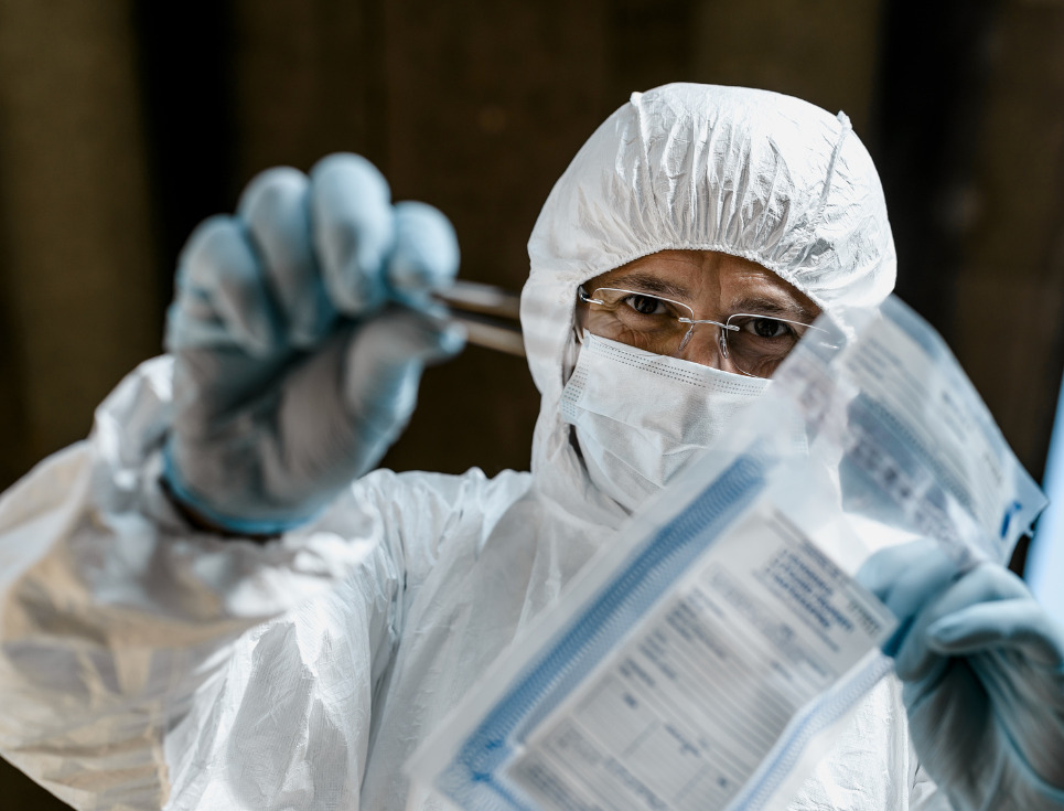 A forensics technician taking evidence at a crime scene and putting it in an evidence bag.