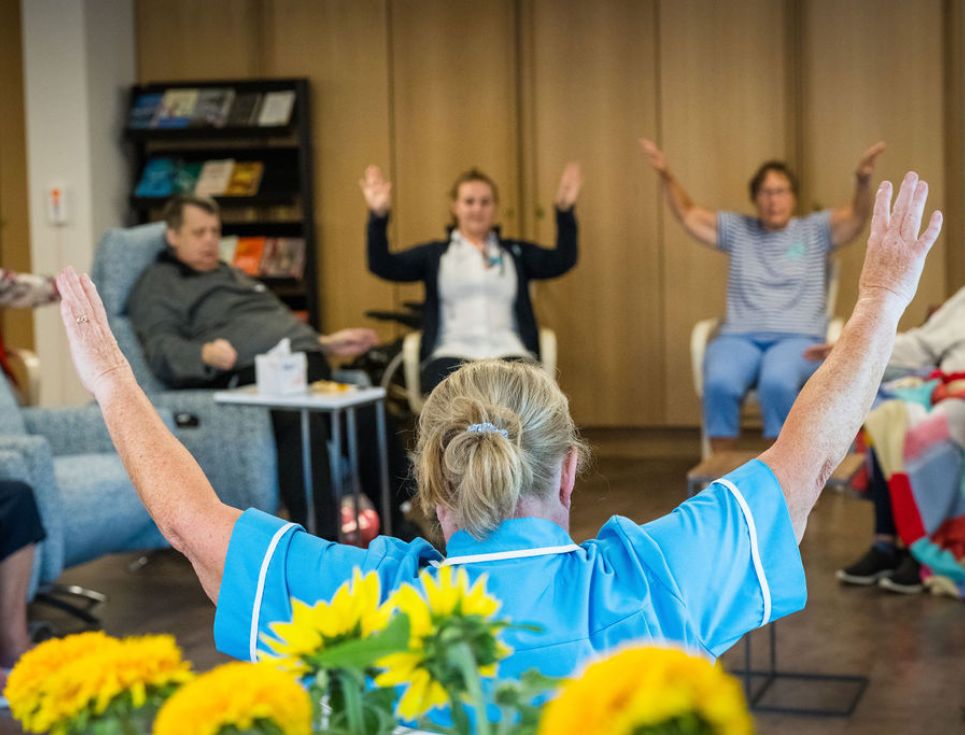 A group of patients, staff and volunteers do a seated tai chi session in the Living Well Centre at St Richard's Hospice