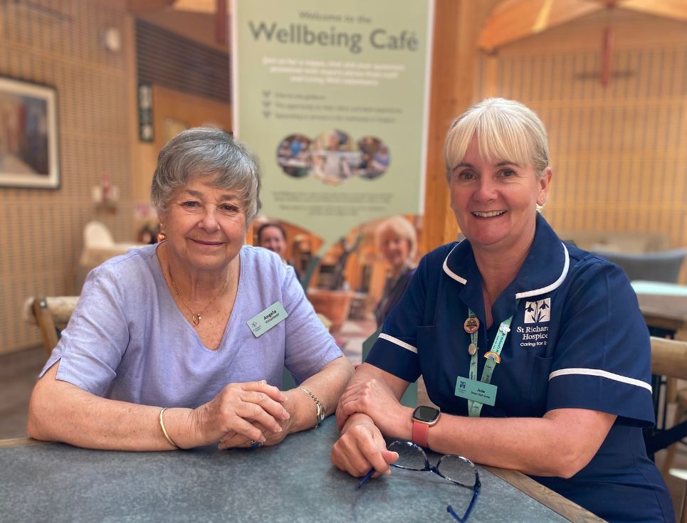 A volunteer and nurse sit side-by-side at a table in the hospice's Wellbeing Cafe.