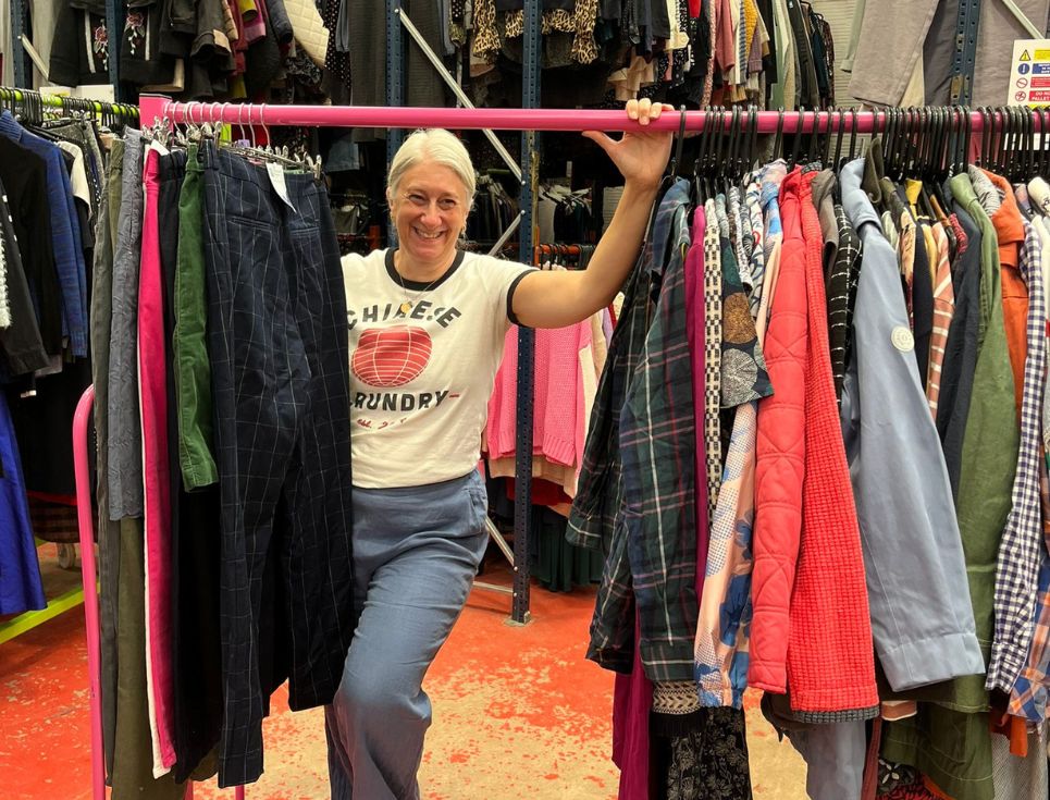 Jen stands with a rail of clothing at the warehouse.